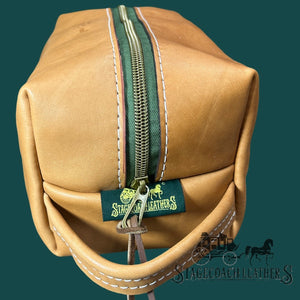 Brown leather dopp kit with green zipper and 'Stagecoach Leather' tag on a dark green background